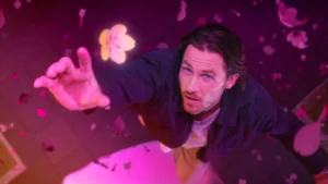 Still frame from 'Master the Market Forces' City Index TVC. Man surrounded by pink light and petals jumps into the air to catch a flower.
