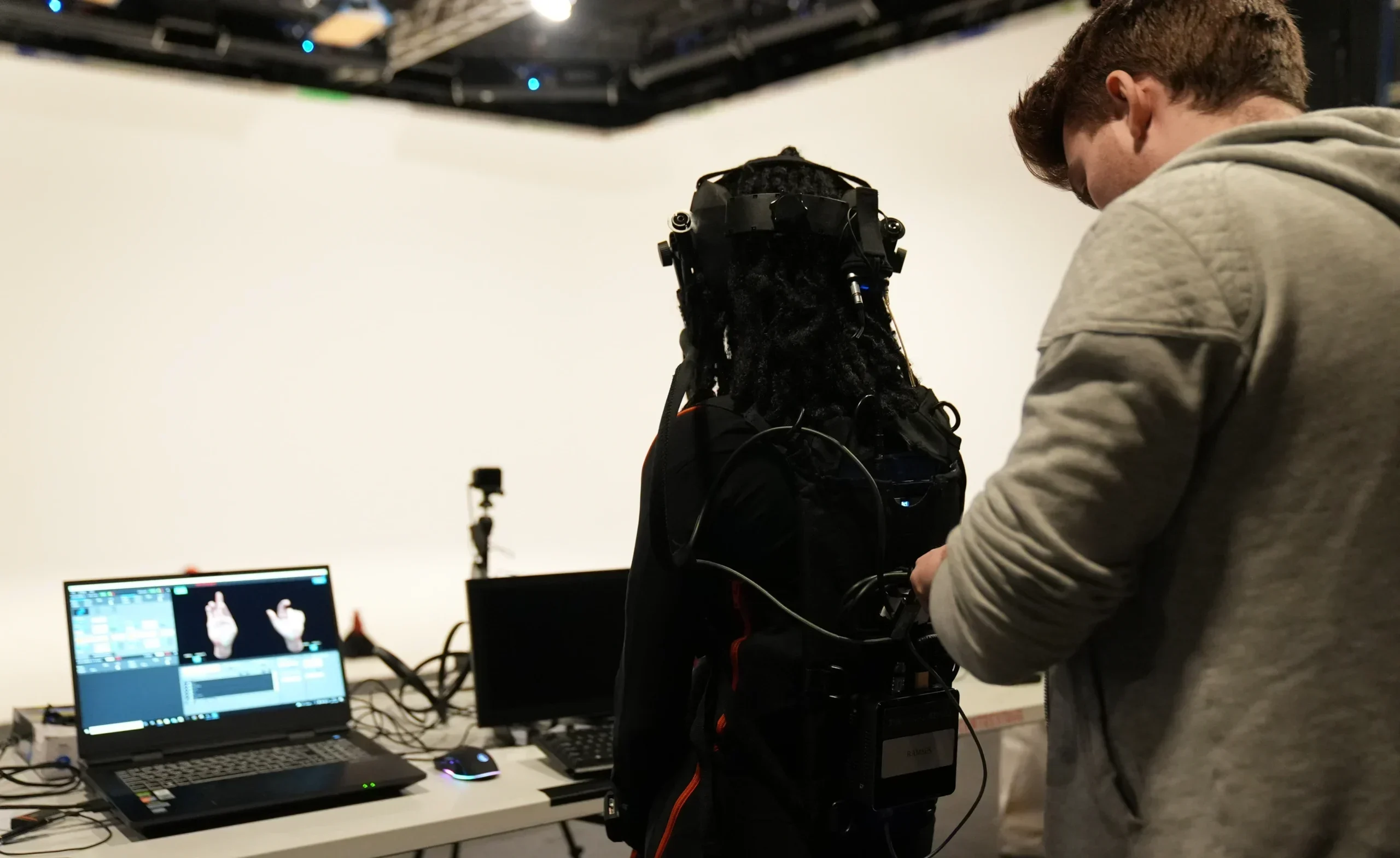 Pebble producer fixing the Grace actor's motion capture equipment. In the background, a laptop is open showing the motion capture of the actor's hands.