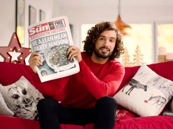 Still frame from our Christmas TVC for The Sun, promoting Joe Wicks' fitness guide. Joe Wicks is sat on a red sofa holding up that week's edition of The Sun newspaper.
