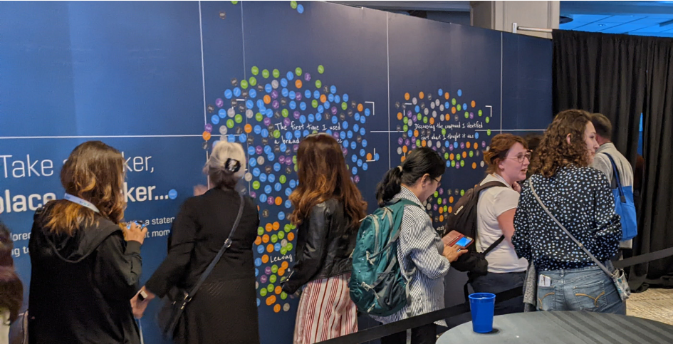 A group of people standing at the entrance to 'The Pursuit' exhibit, some reading the exhibit stand.