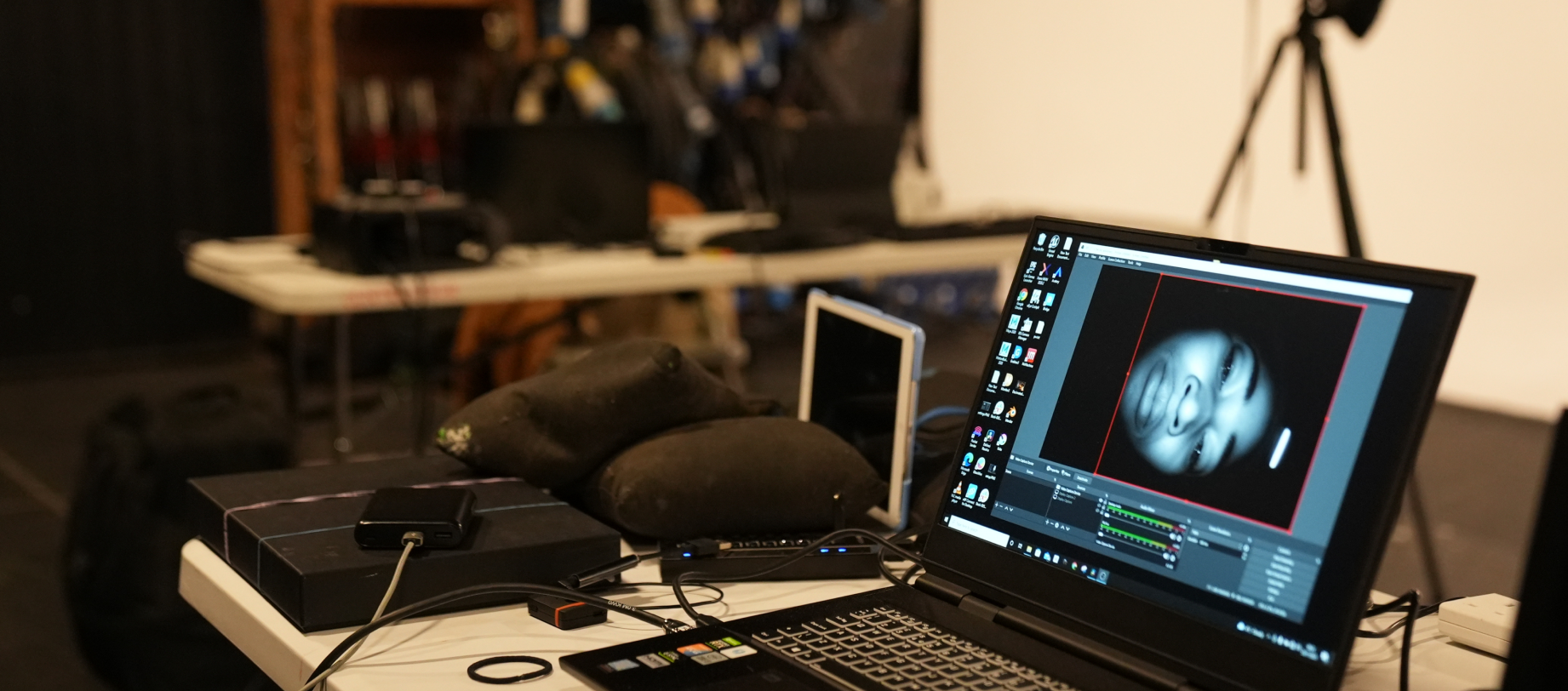 An open laptop on a table with lots of filming/tech equipment. On the laptop screen, a close up feed of the Grace actor's face can be seen open in a piece of software.