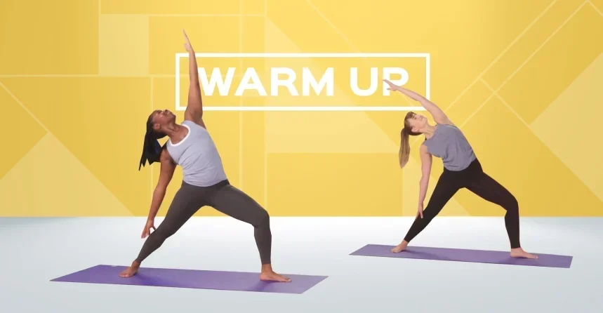 2 women doing yoga pose 'warrior two' in a green screen environment: plain white floor with a yellow wall, with the words 'warm up' in white in the centre