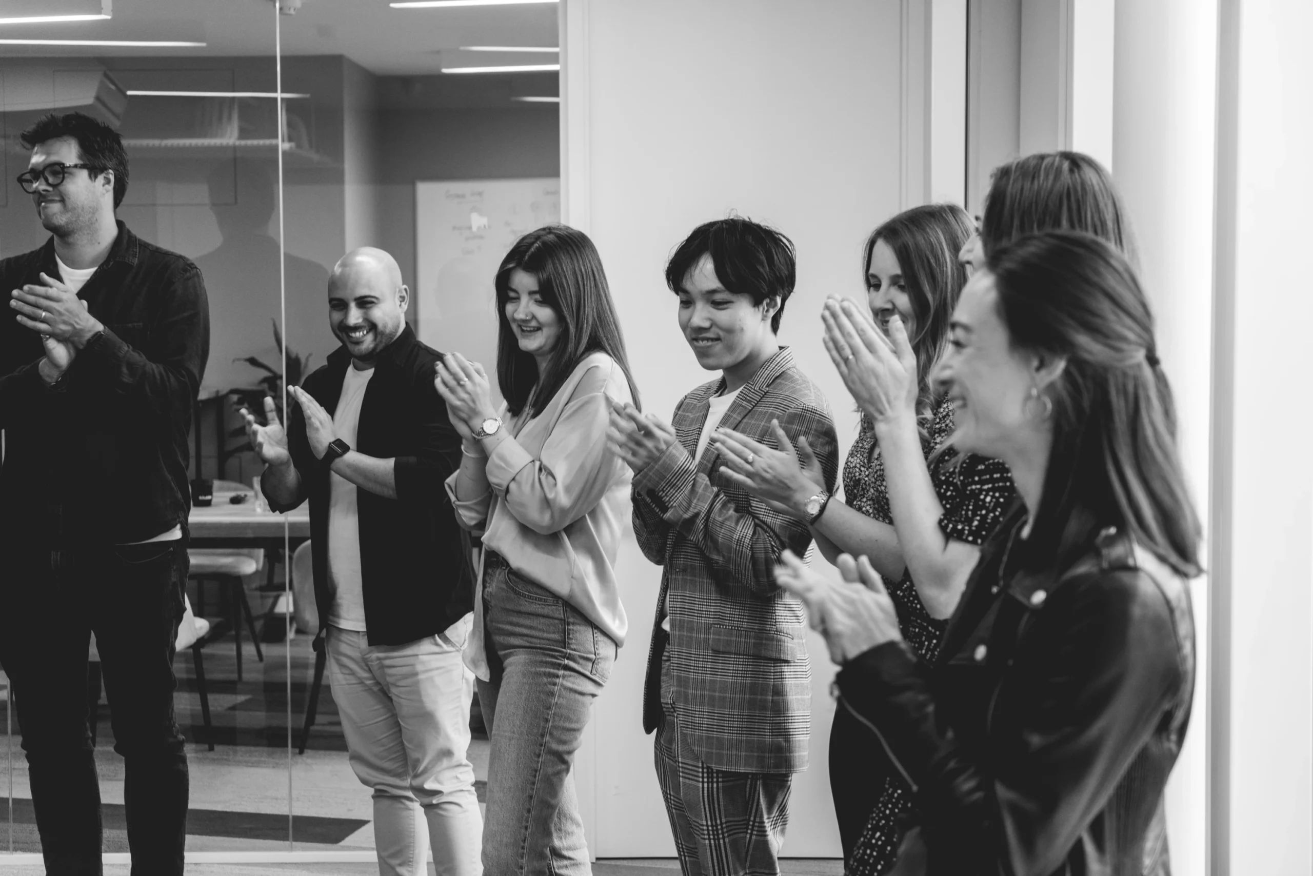 Black and white photo of the Pebble team stood clapping after a presentation in our office.